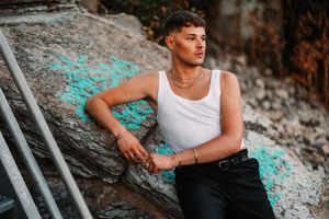 Person in white tank top poses against rocky natural backdrop during outdoor photo session.