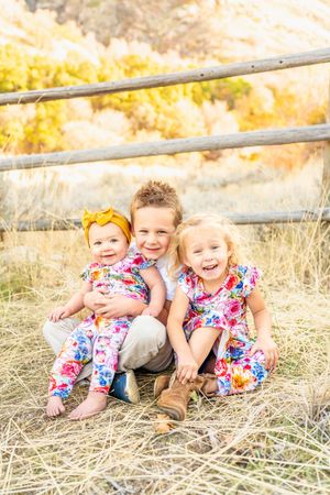 Three children sitting together in matching floral outfits by rustic fence at Hidden Valley Park.