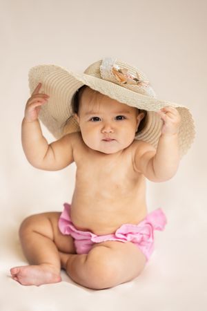 Baby holding a large sun hat in studio in Saratoga Springs.