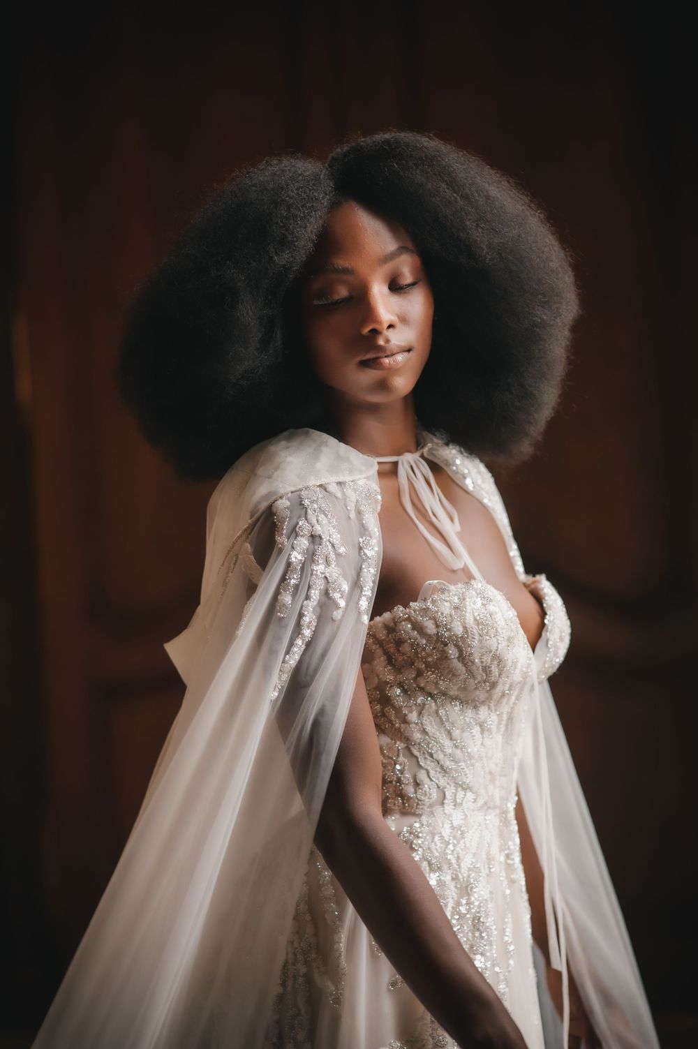 A bridal portrait showcasing an elegant white wedding gown with lace details and flowing cape.