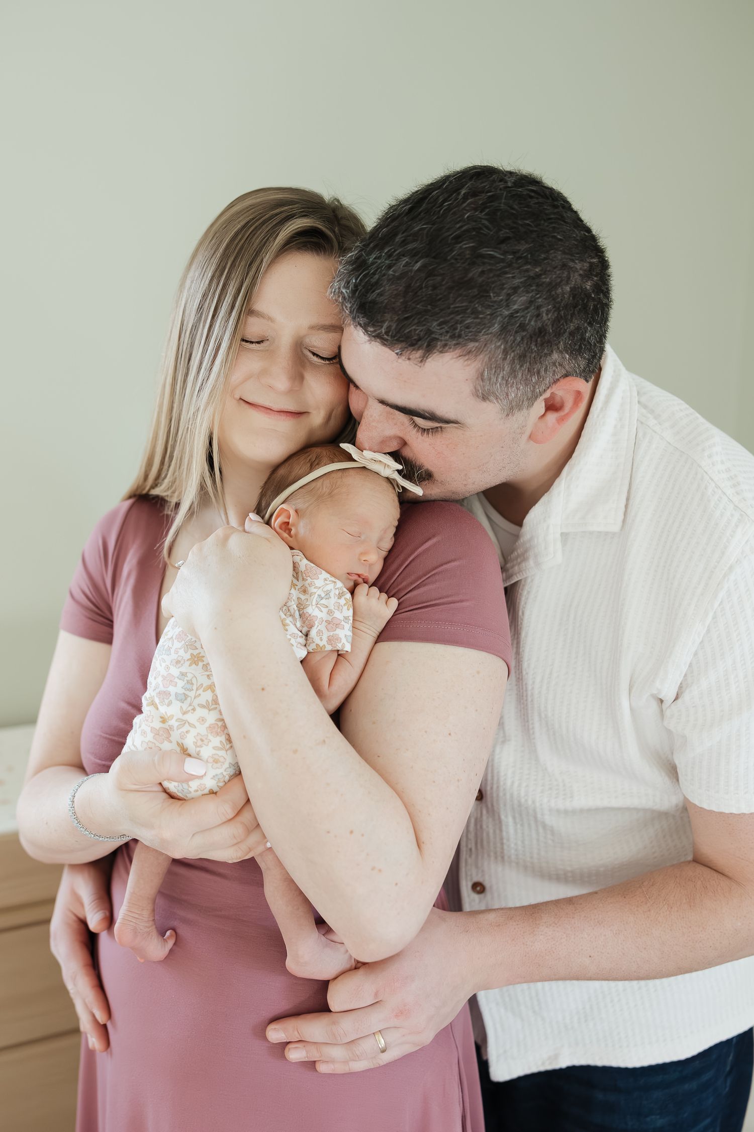 newborn photography kansas city mo mom holding newborn baby girl husband standing over shoulder giving baby girl kiss on head