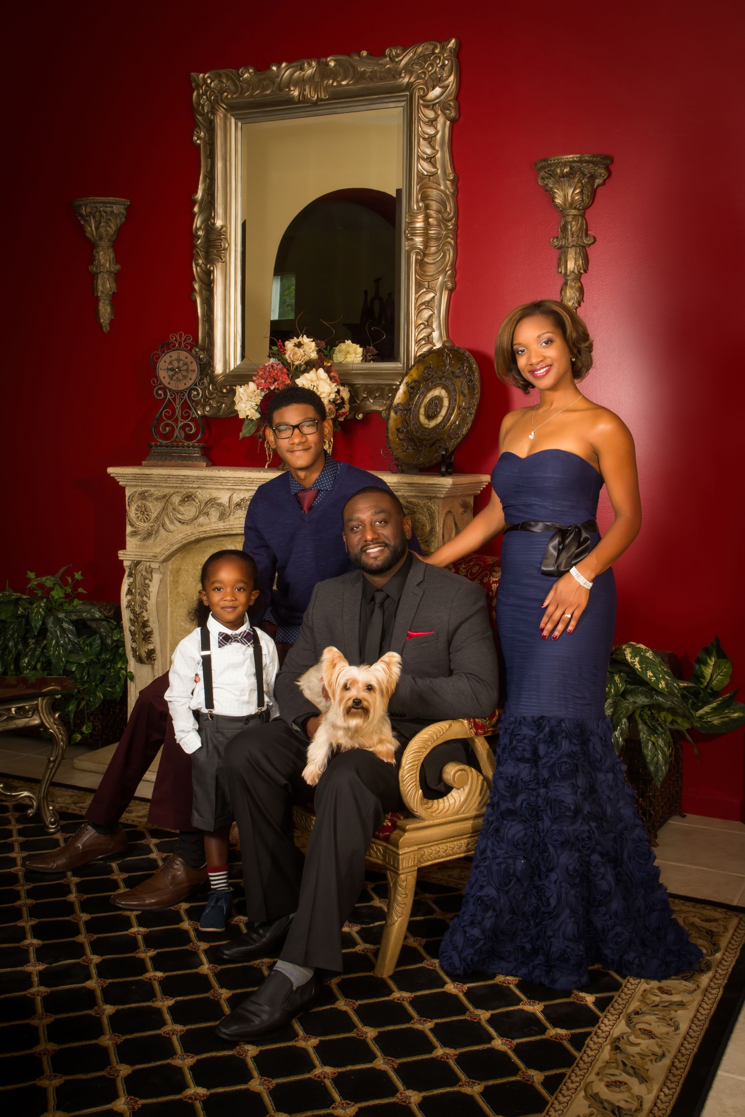Family portrait session in an elegant room with red walls and ornate gold-framed mirrors.