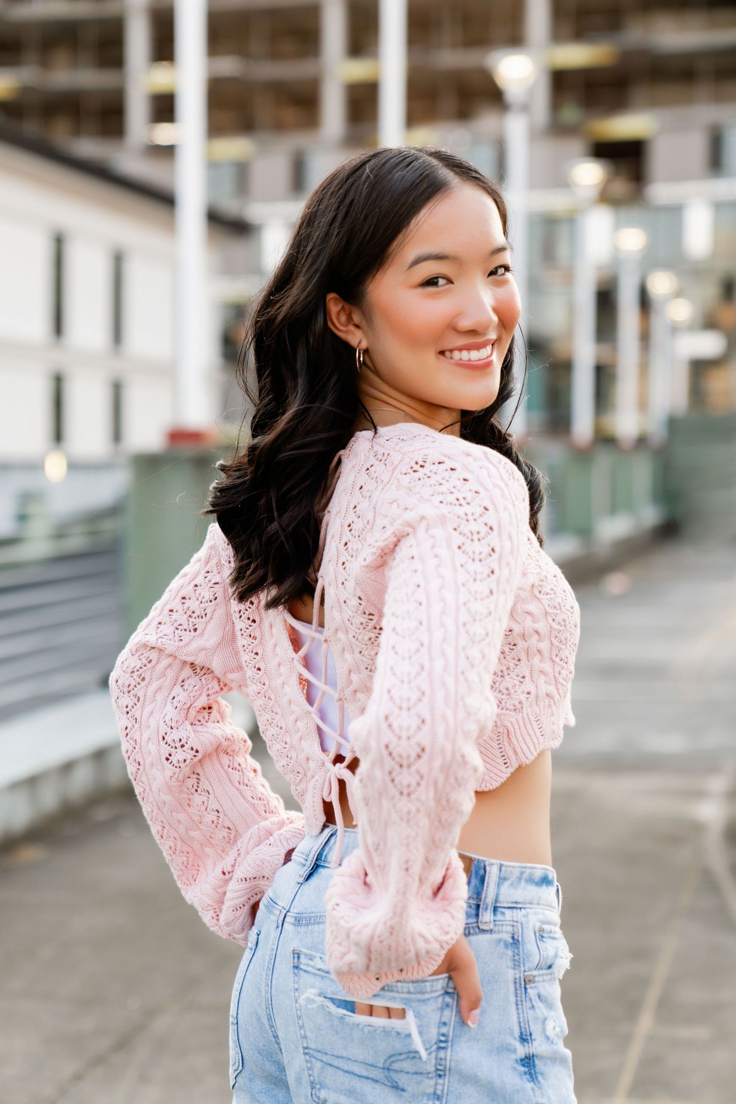 High school senior smiling in a pink sweater and denim on a rooftop at golden hour – stylish and modern senior portrait photography.