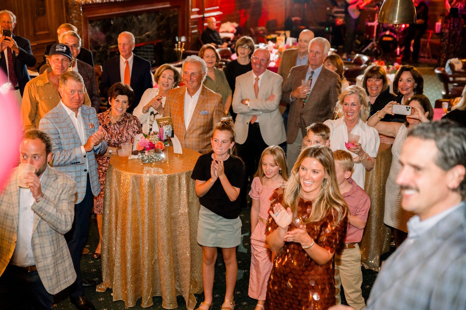 Large group of elegantly dressed guests celebrating at an indoor evening party with floral centerpieces.