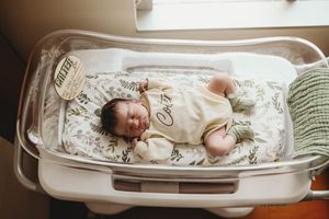 A newborn baby rests peacefully in a hospital bassinet with floral pattern bedding.