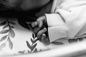 Black and white close-up of tiny baby fingers grasping against a textured background.
