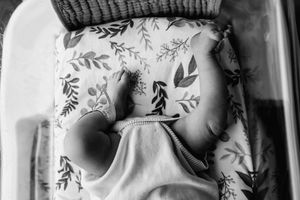 Intimate newborn photography session showing tiny hands and delicate details against soft white bedding.