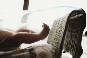 Newborn baby resting peacefully on textured bedding with natural window light.
