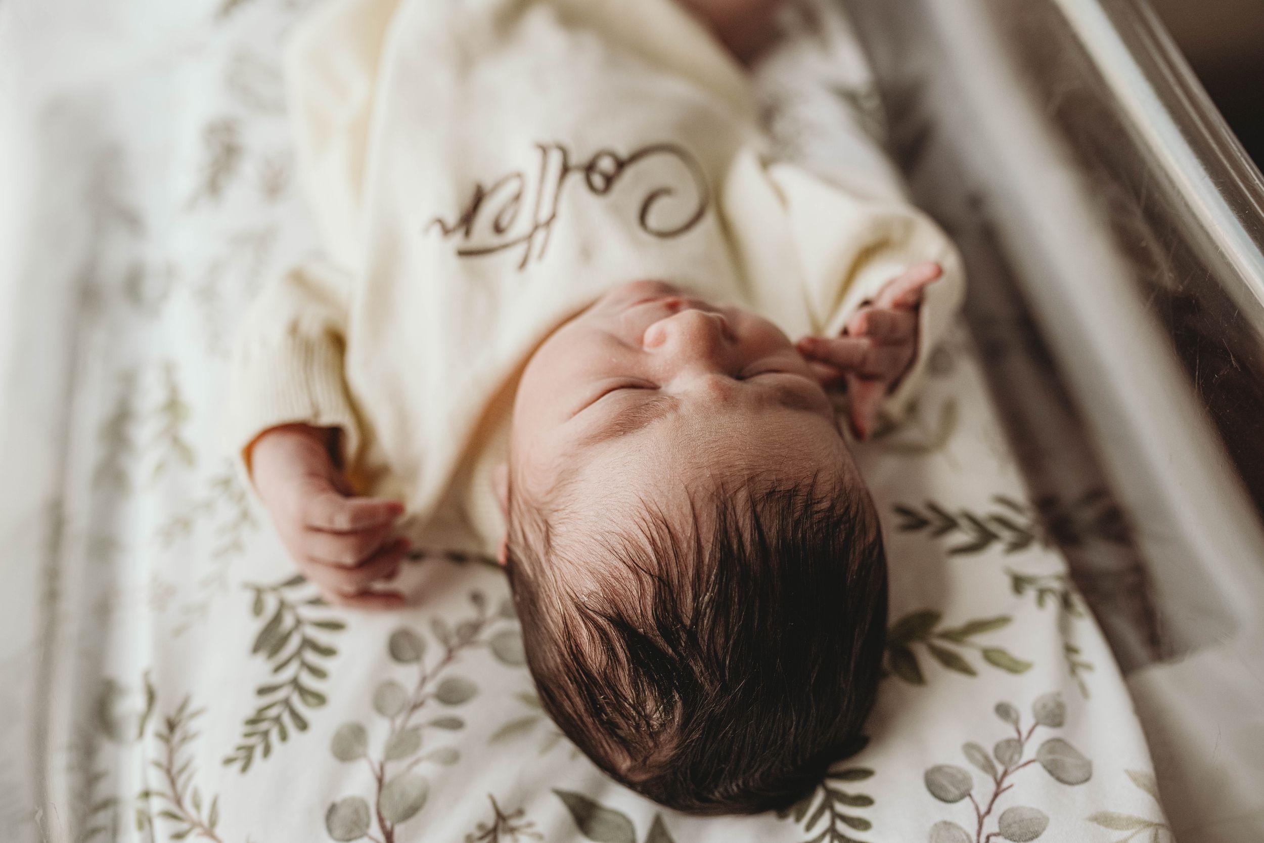 Baby lying on white bedding with delicate floral pattern details.