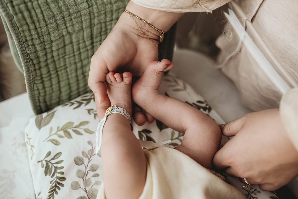 Gentle hands holding newborn baby against soft textured fabrics.