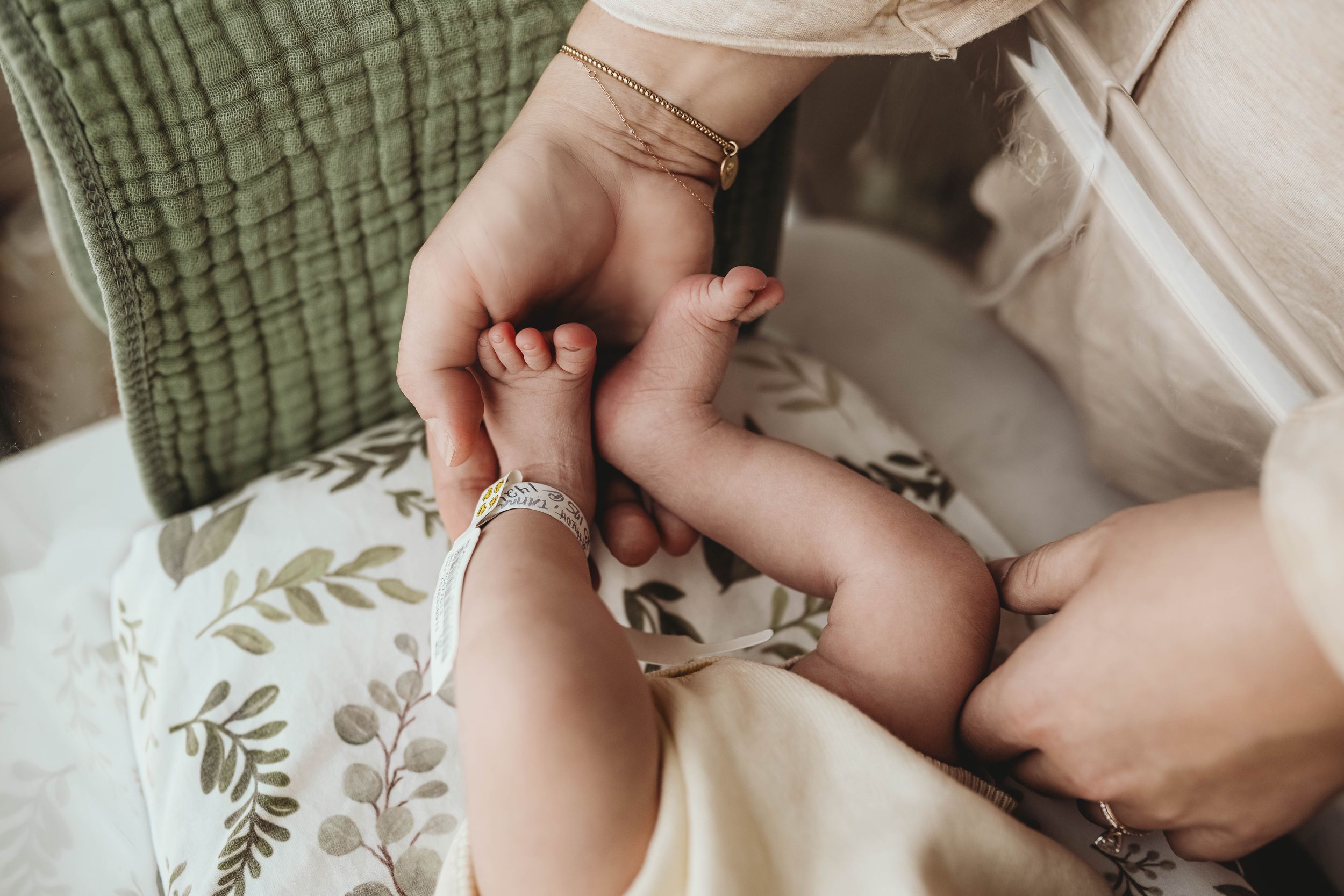 Gentle hands holding newborn baby against soft textured fabrics.