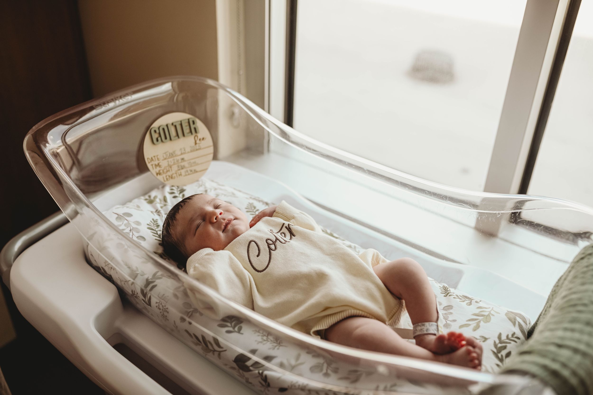 Newborn baby resting on changing table near window with natural lighting.