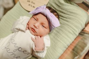 Sleeping newborn wearing soft purple headband on mint green pillow.