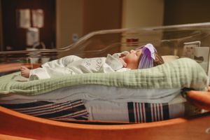 Professional newborn photography setup with baby on cushioned surface.
