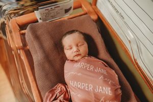 Newborn resting peacefully on personalized brown blanket during photo session.