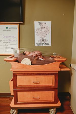 Newborn photo session on wooden changing table with medical center signs visible.