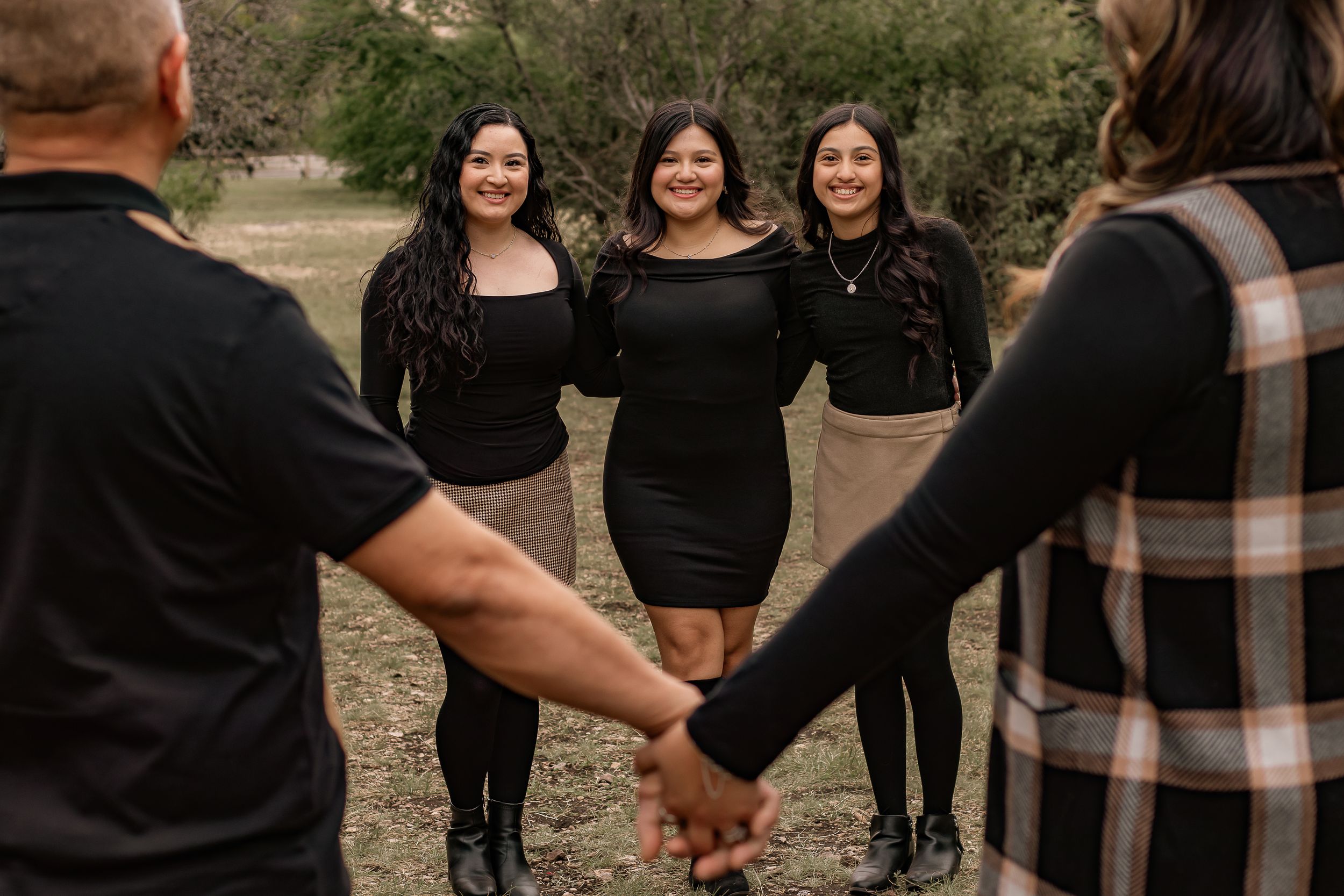 Three young women in black outfits smiling together during an outdoor family photo session.