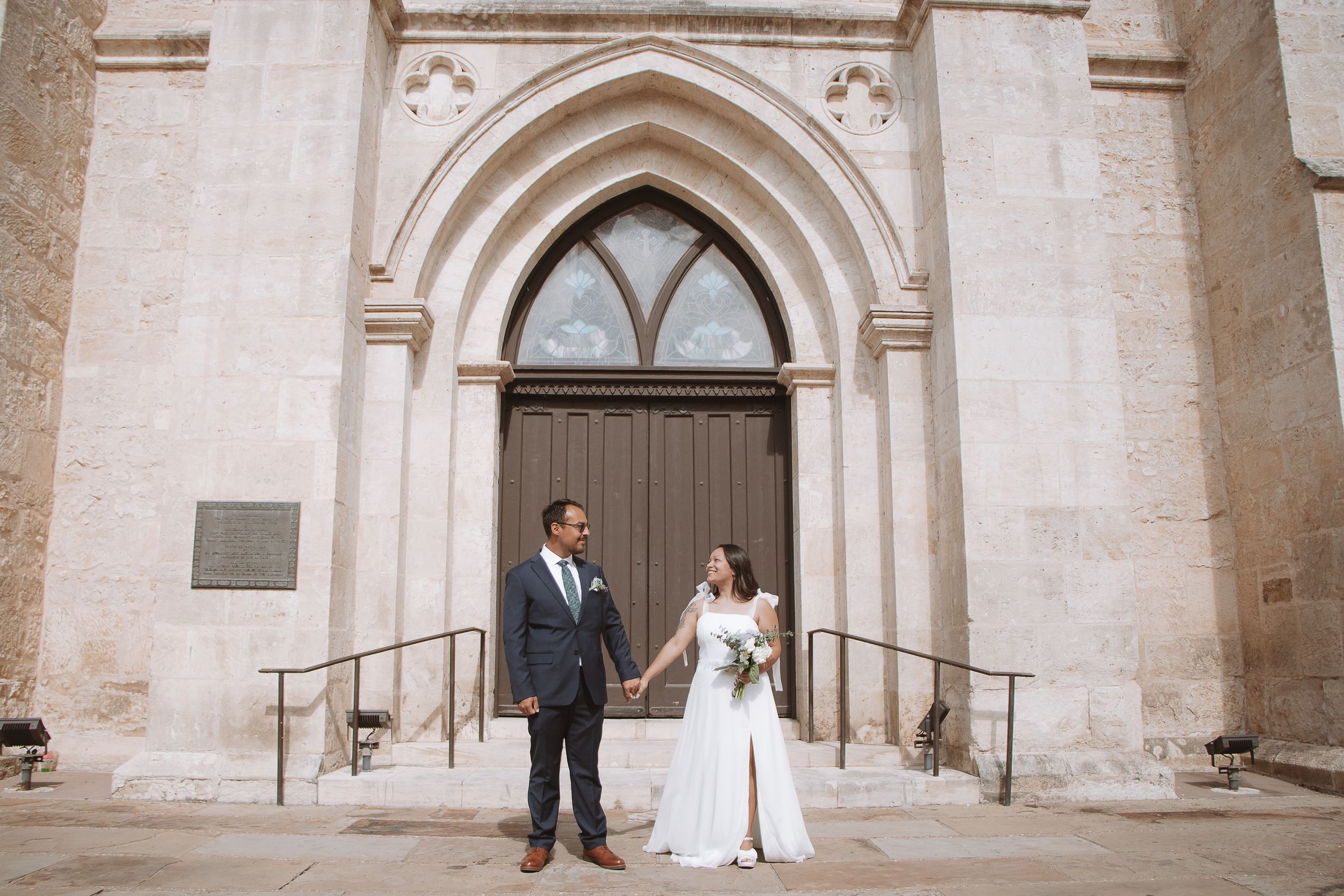 Bride and groom holding hands outside a stone Gothic church on their wedding day.