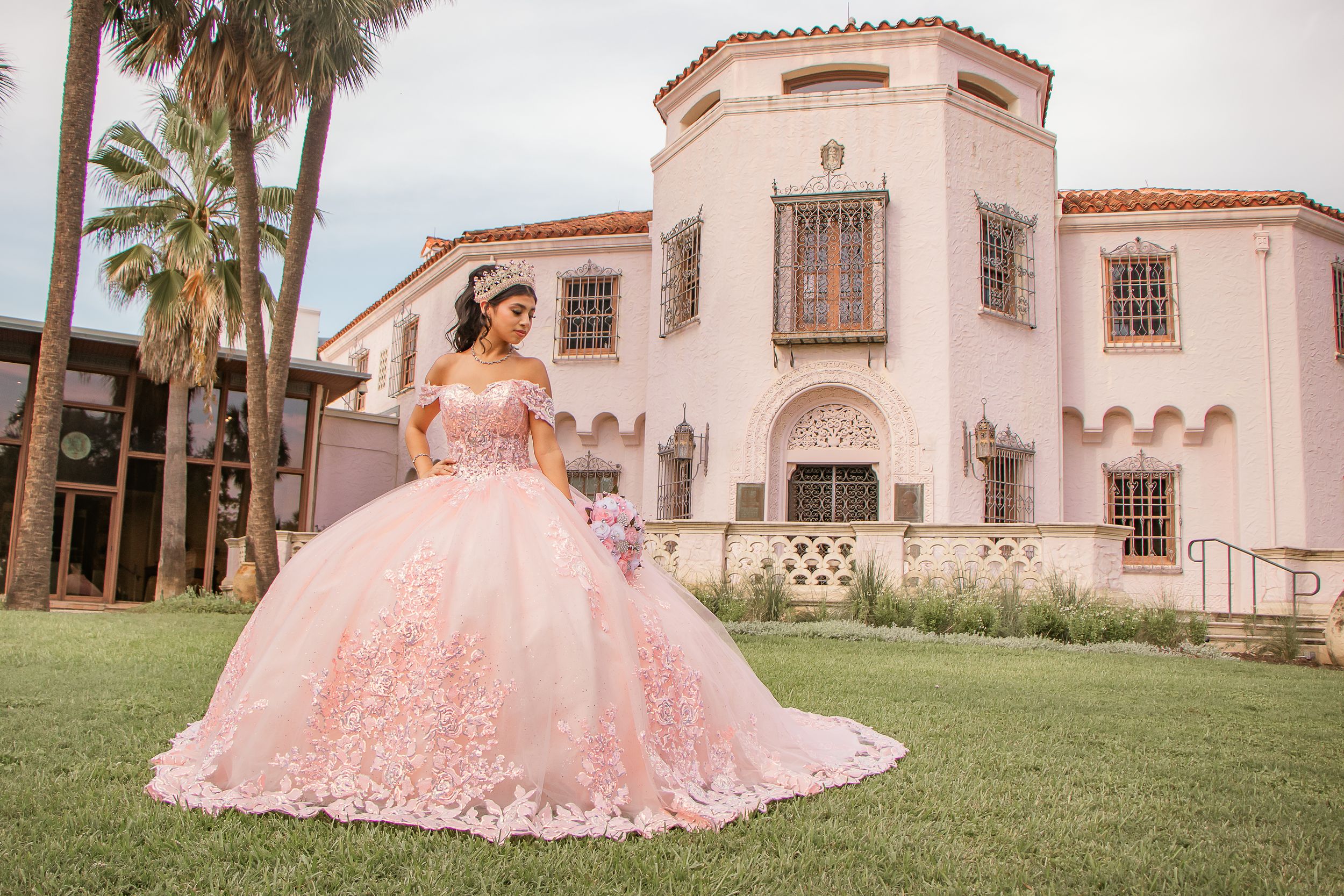 Young woman in elegant pink quinceañera ball gown posing in front of a grand building.