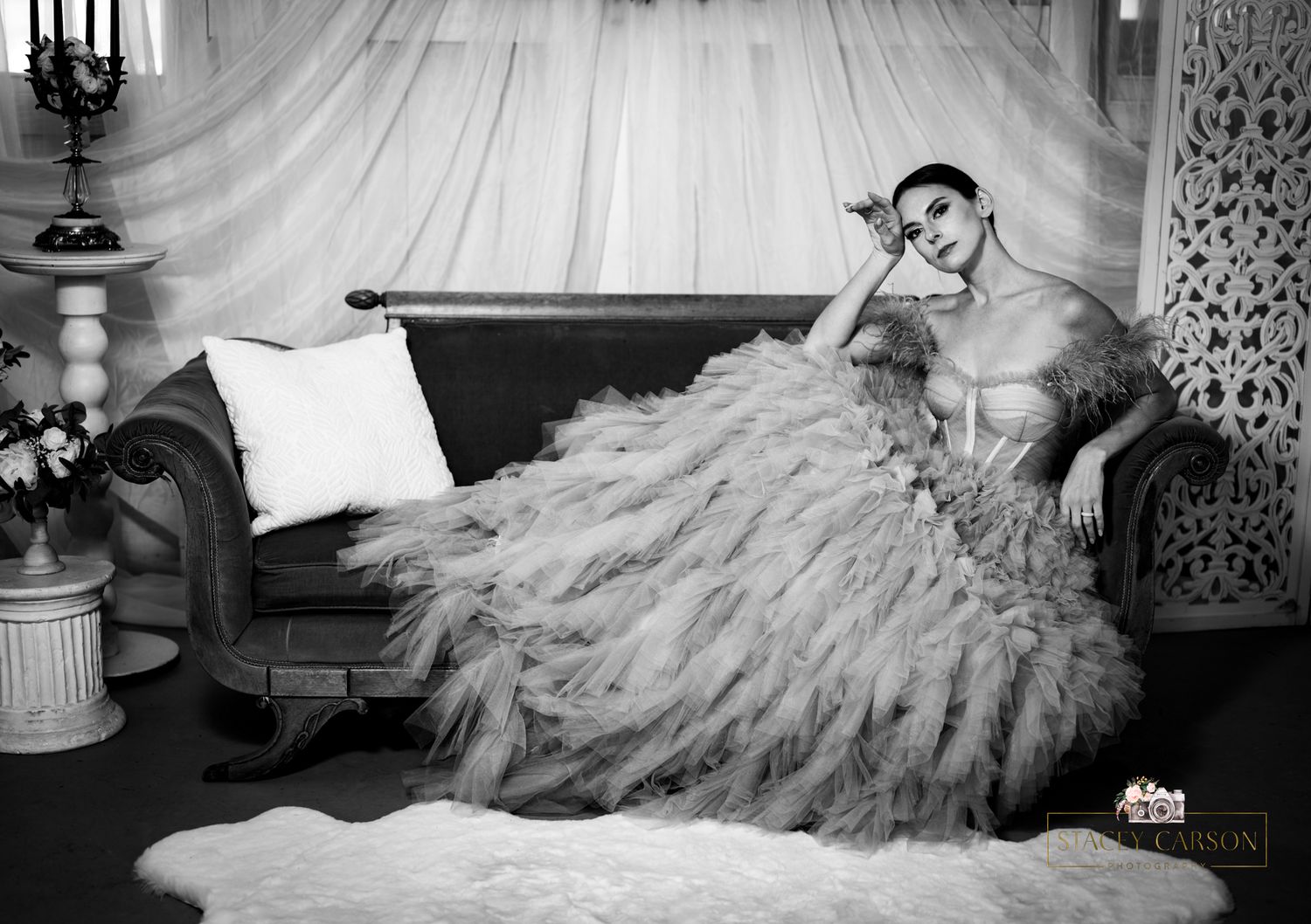 A dramatic black and white photo of a woman posing on a couch in an elaborate ruffled gown.