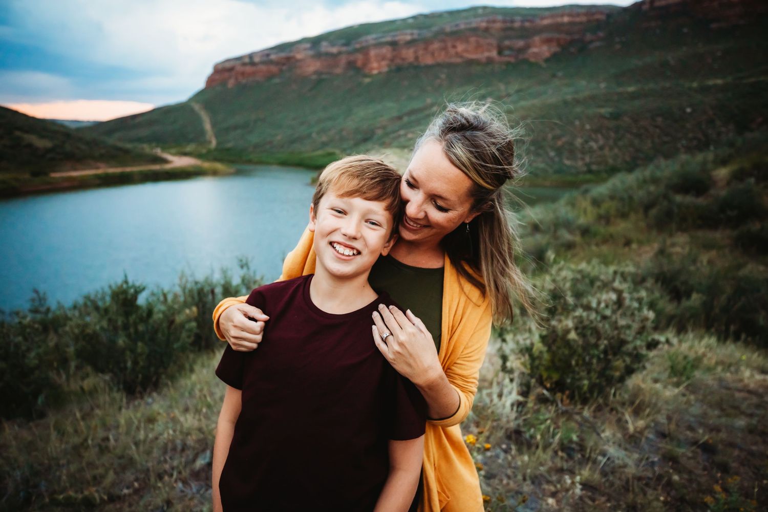 Mom has hands on son's shoulders while they smile with lake and mountain in the background in Dickson, TN