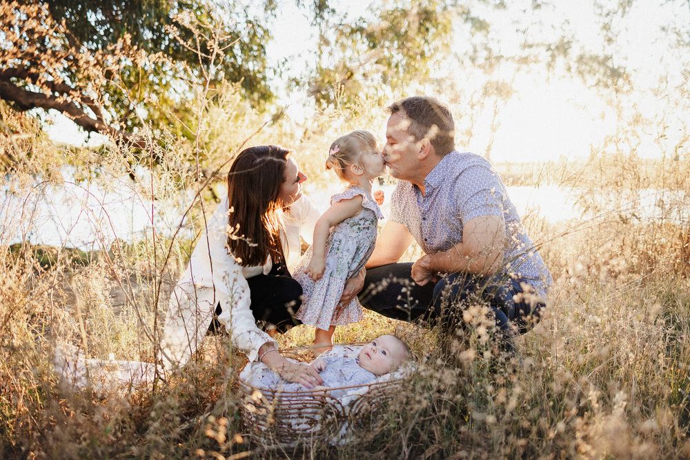 Family sits together in tall golden grass during sunset for outdoor portrait session.