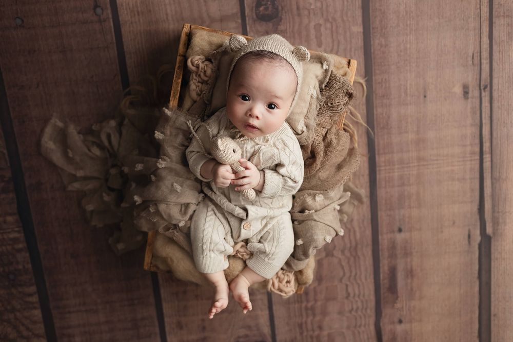 A baby wearing knit clothing lies on textured fabric against a rustic wooden background for a photoshoot in Perth, WA.