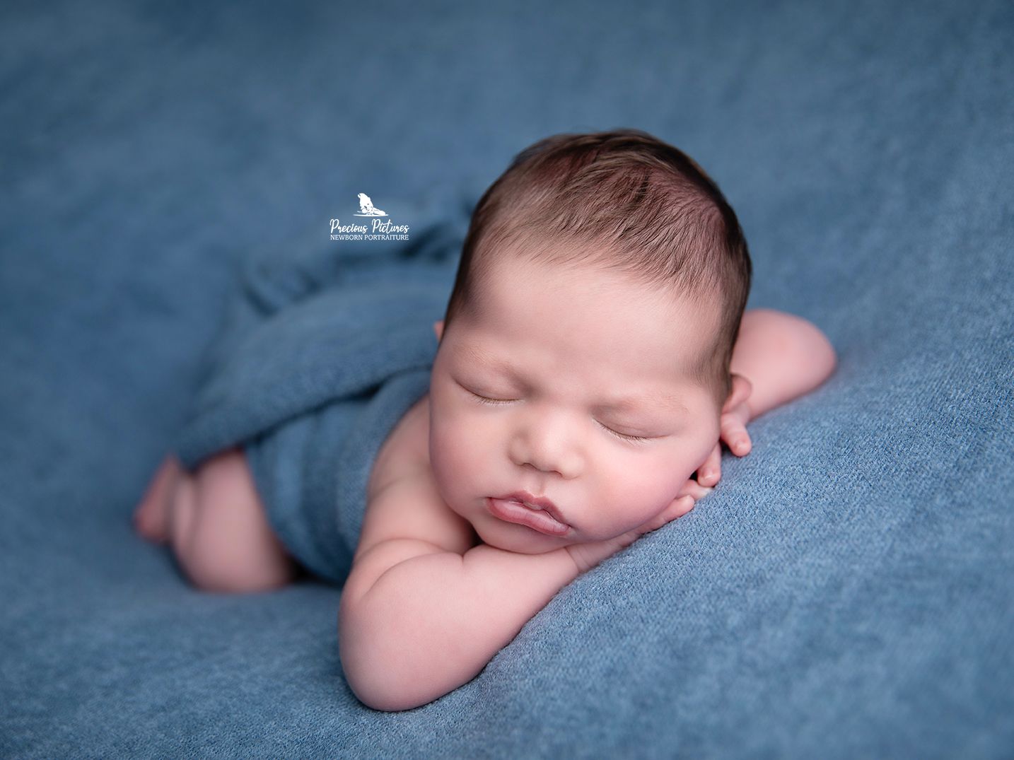 Peaceful sleeping newborn baby boy on a soft blue textured backdrop, professional newborn portraiture at Precious Pictures, Rabat, Malta.