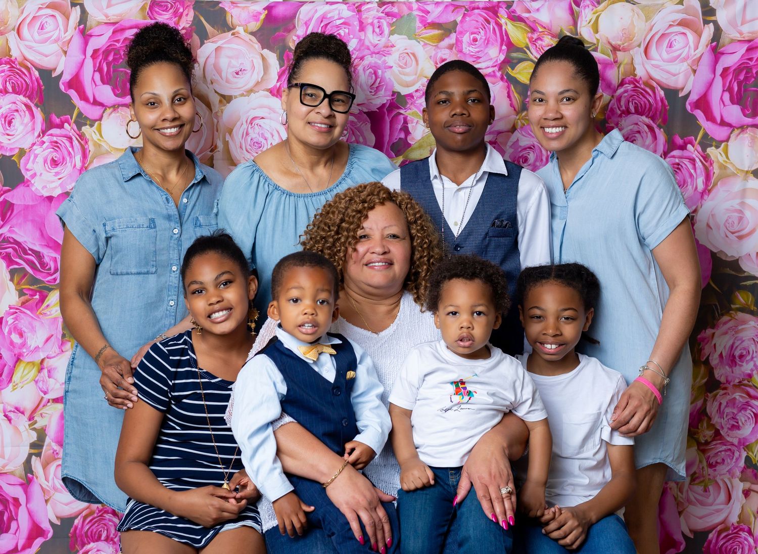 A happy family poses together in front of a pink floral backdrop for professional portraits.