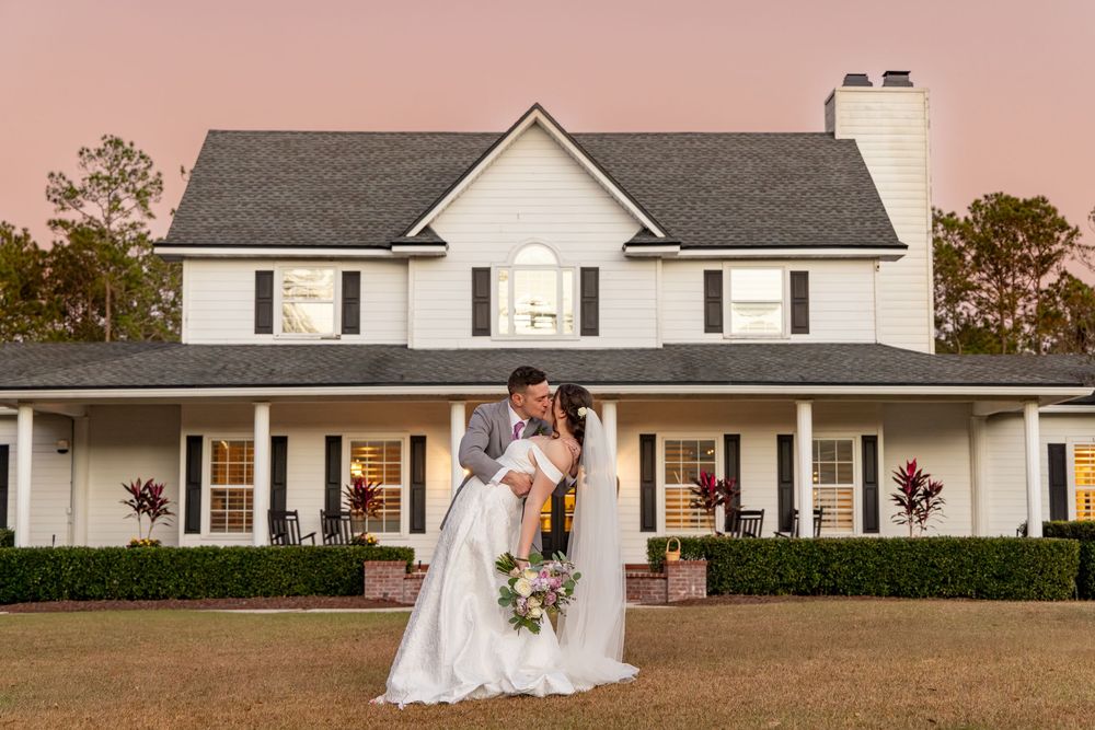 White farmhouse style venue with classic columns and wrap-around porch creates an elegant backdrop for outdoor events.