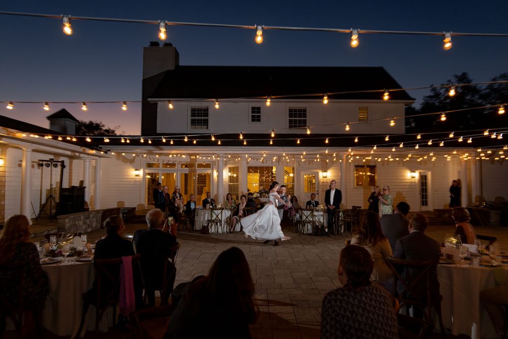 String lights illuminate an outdoor wedding reception venue with tables and chairs set up under the night sky.