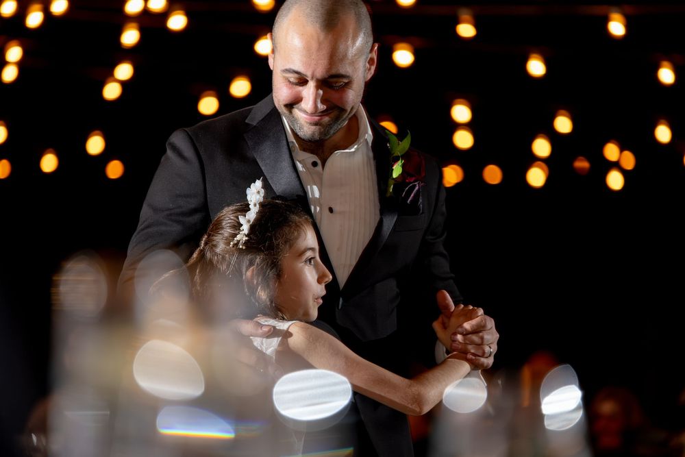 A couple shares a romantic dance together under twinkling string lights at an evening celebration.