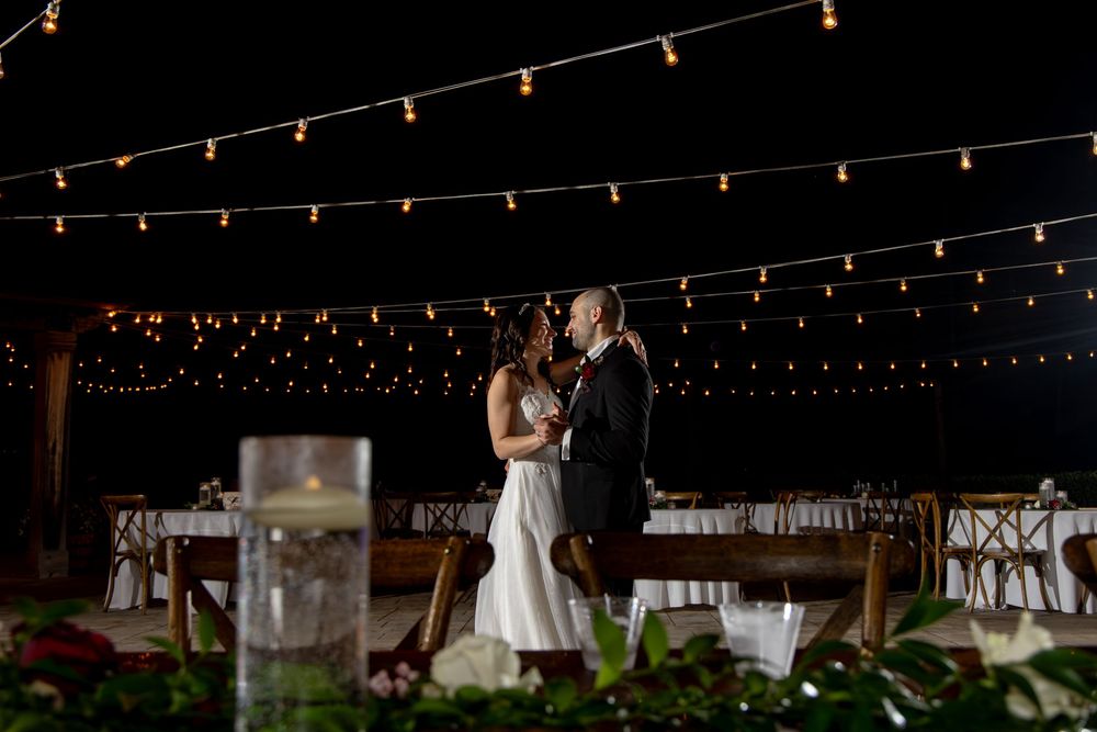 String lights illuminate an outdoor wedding reception area with a rustic barn-style setup at night.