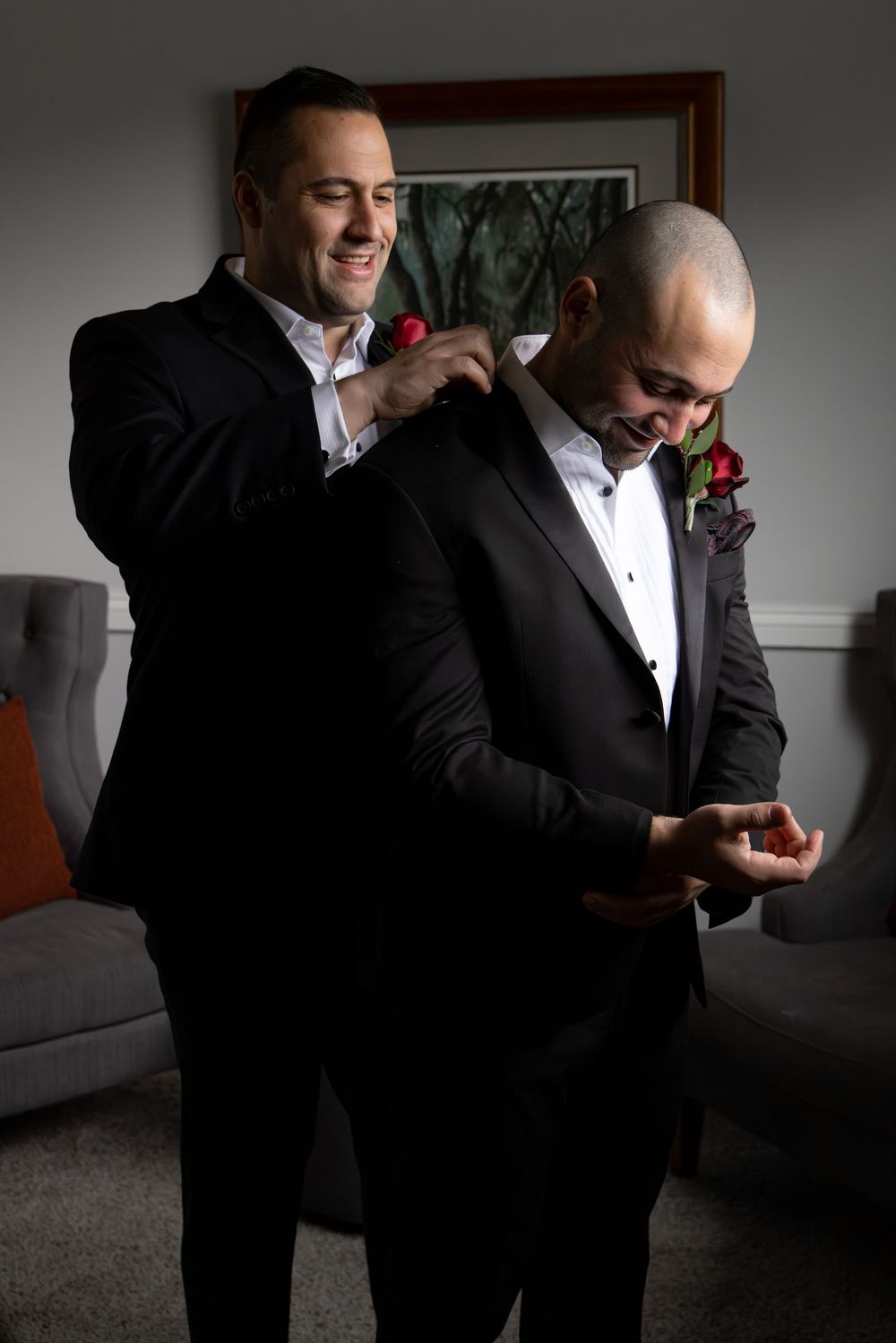 Two men in black tuxedos share a lighthearted moment while getting ready for a formal event.