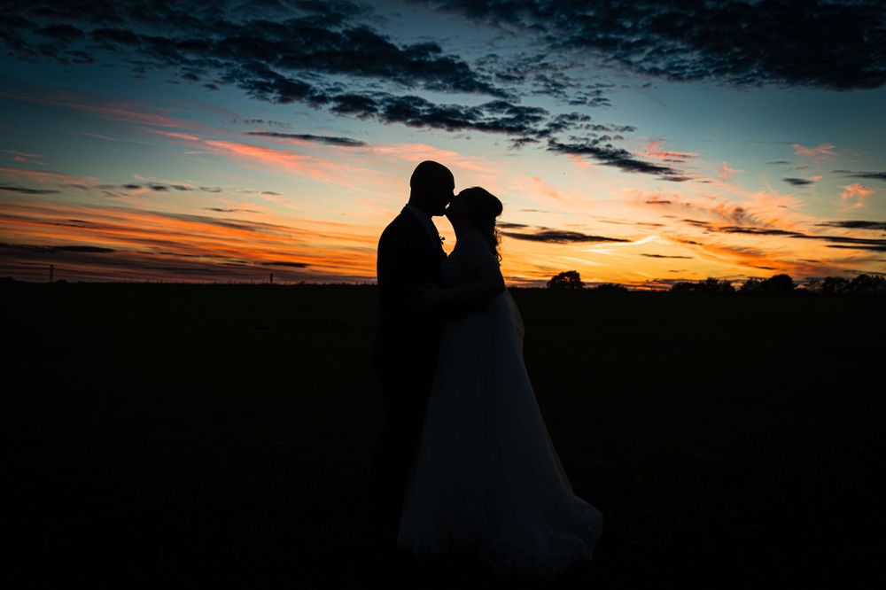 Two silhouetted figures stand close together against a colorful sunset sky with dramatic clouds.