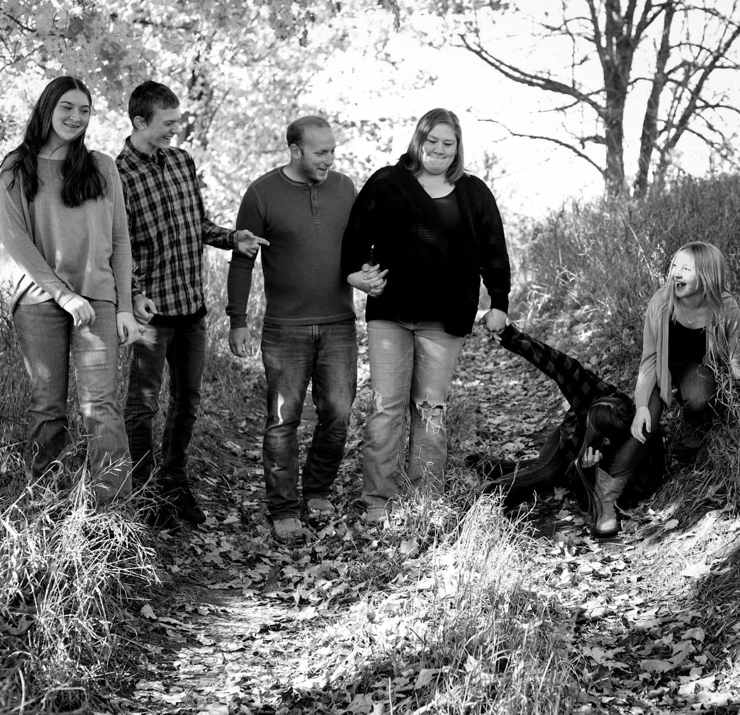 Family group walking together on wooded path in black and white photography.