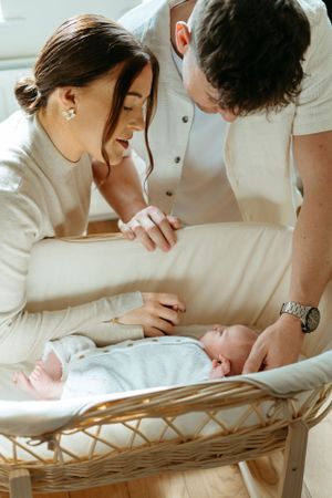 Parents leaning over a wicker bassinet to admire their newborn.