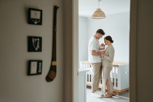 Family standing in a nursery with natural light streaming through windows.