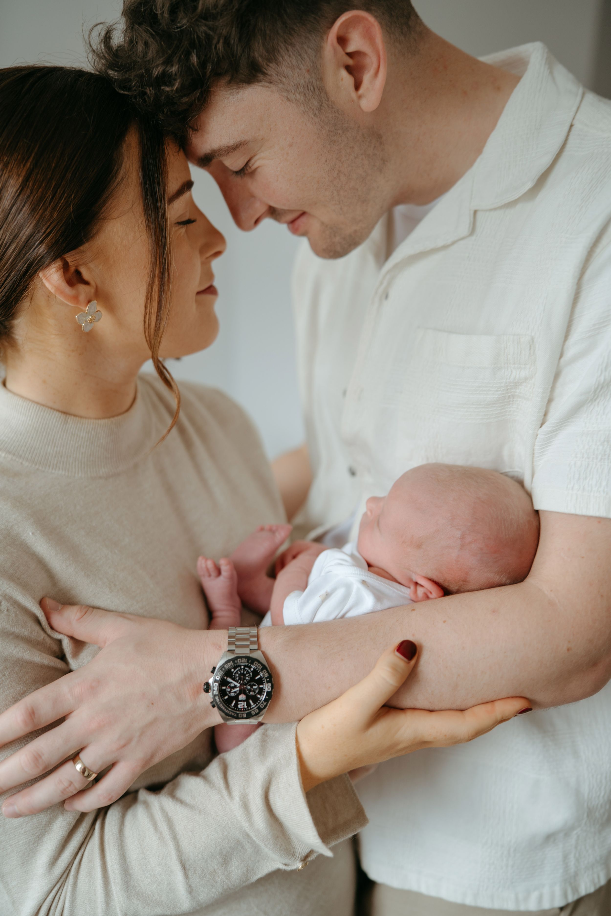 Parents sharing loving moments with their newborn baby in a minimalist white setting.