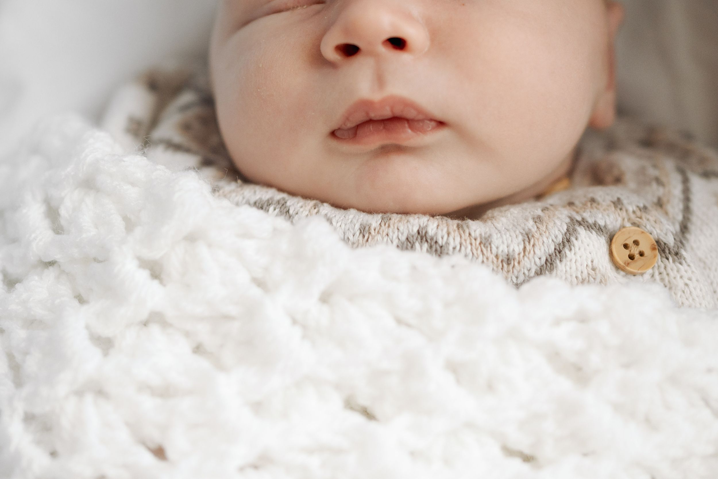 Close-up view of a sleeping newborn baby's face nestled in soft white fabric.