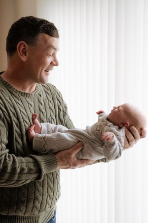 Person in green cable knit sweater holding and gazing at a newborn baby.