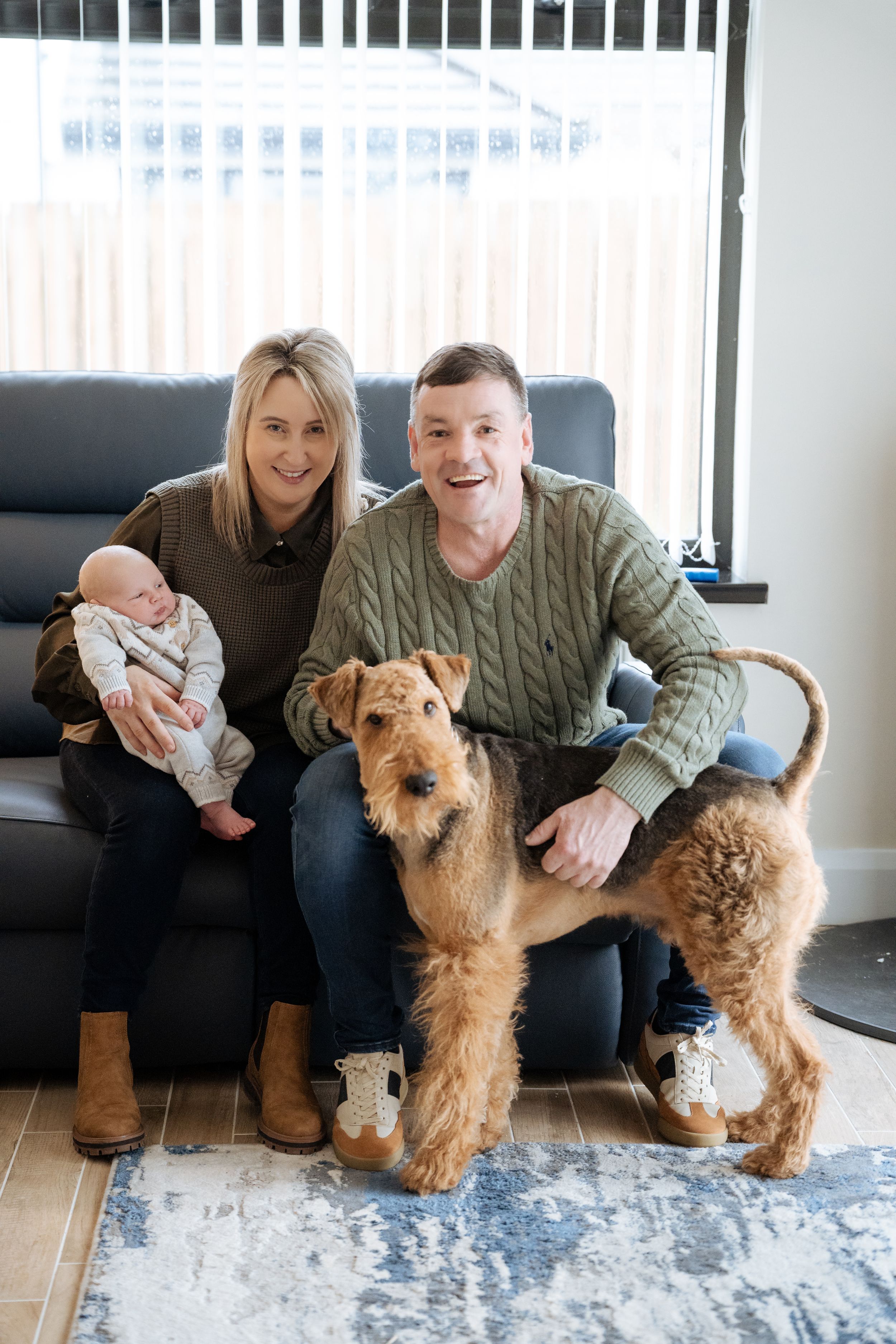 Family sitting on floor with their two terrier dogs and newborn baby.