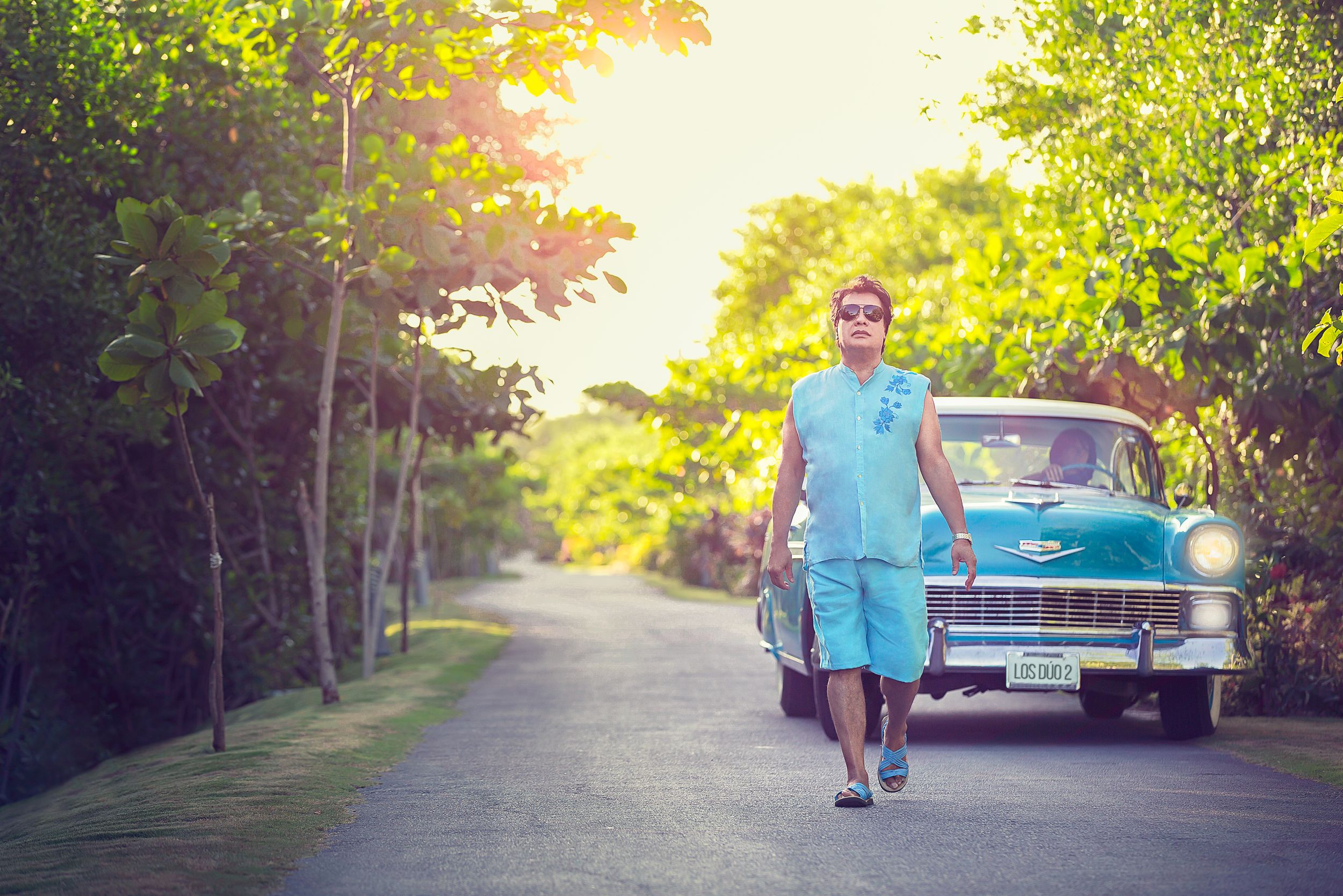Family portraits taken at sunset in a tree-lined driveway with a classic blue vintage car.