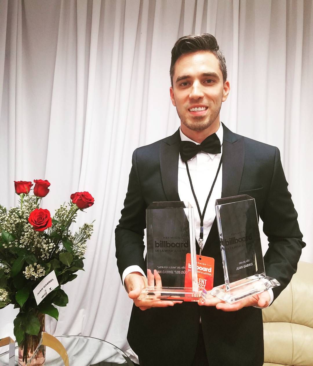 Professional in a dark suit holds an award plaque at a formal event with red roses in background.