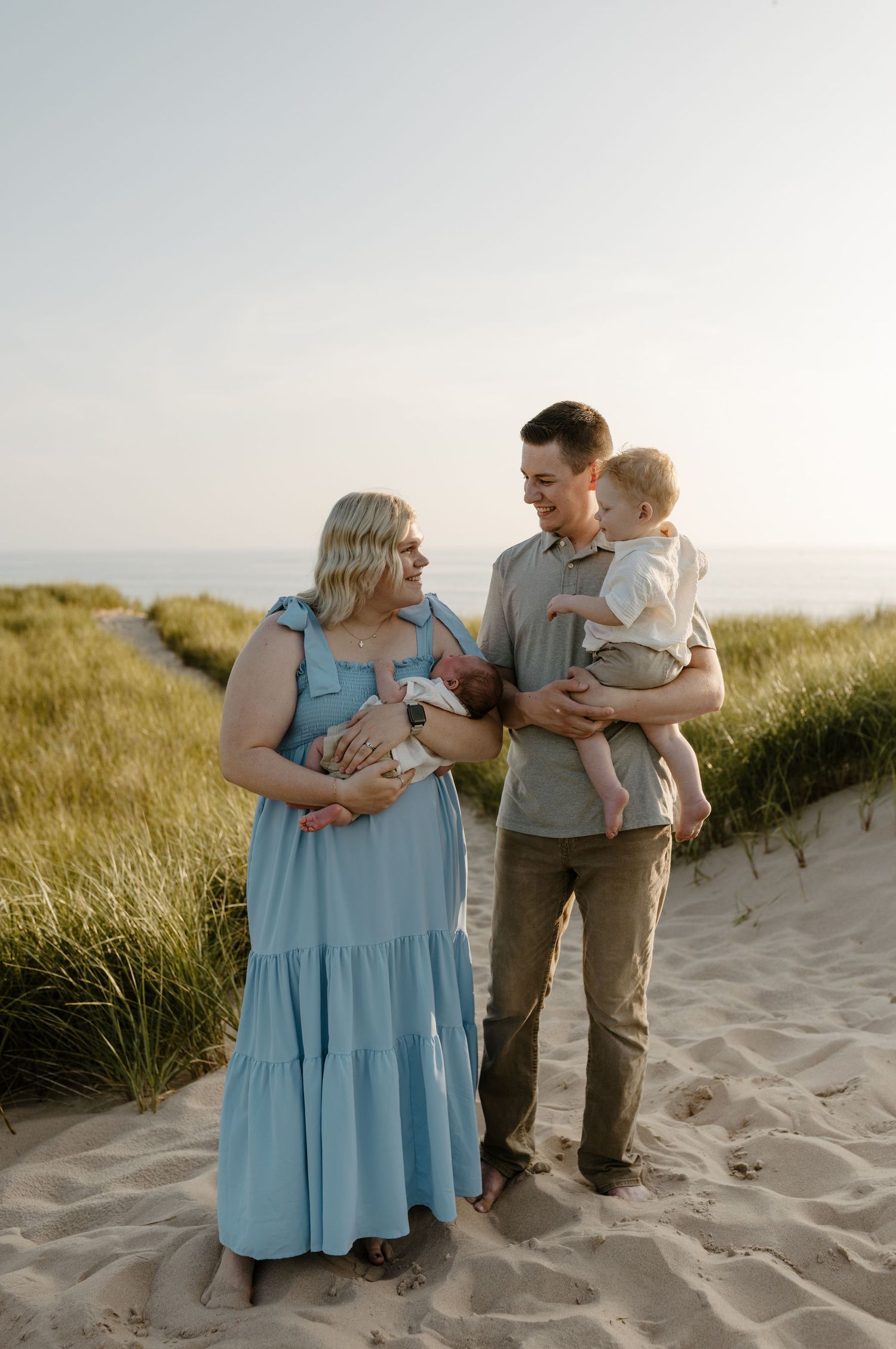 A family of three, including a pregnant woman, walking together on a sandy beach during sunset. Fort Worth Texas family photographer.