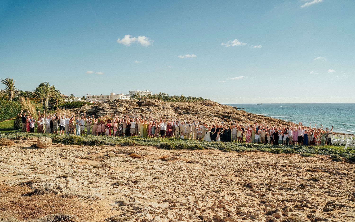 Wedding party celebrates with raised arms under an arch on a hilltop in black and white photography.