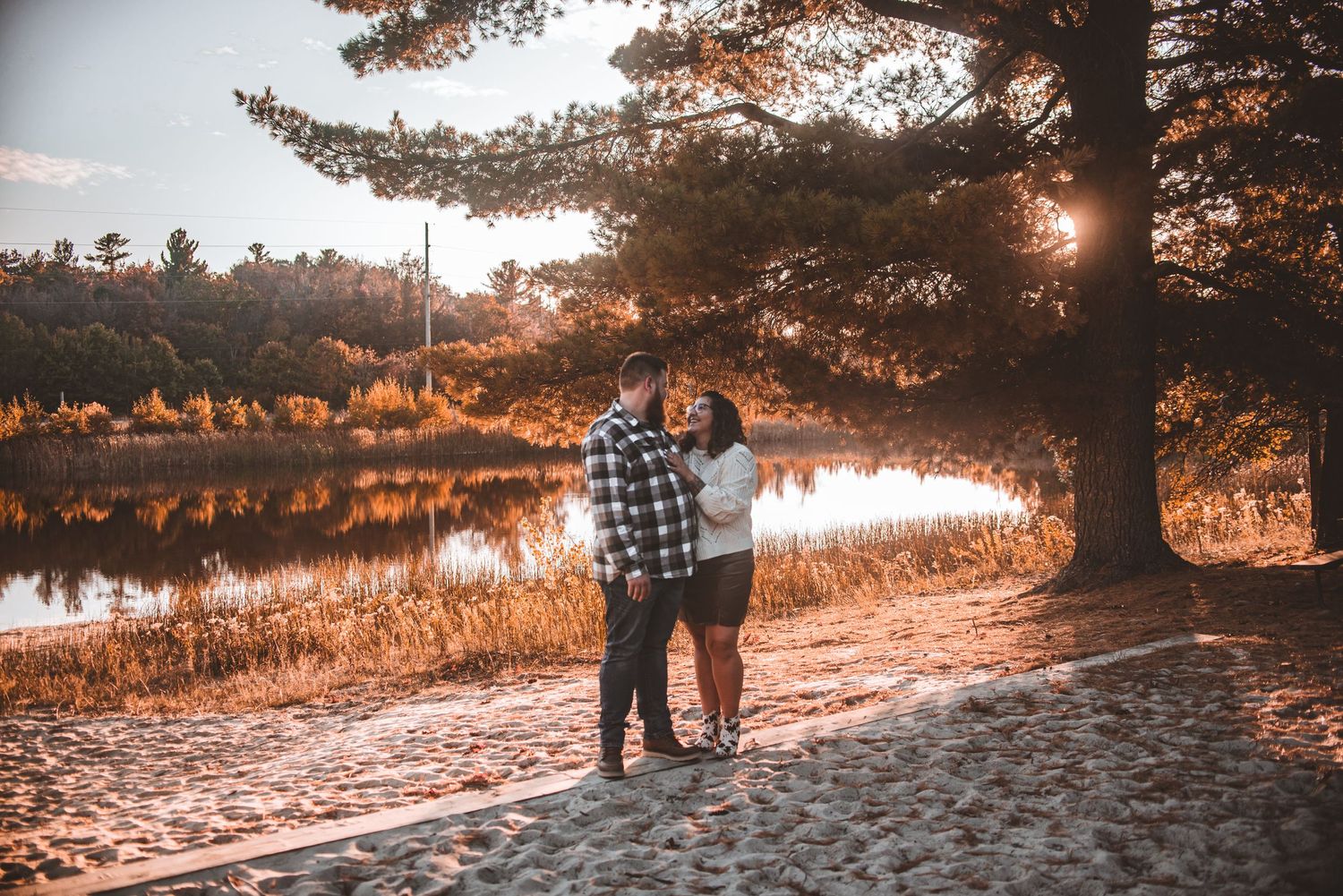 Couple silhouetted against a lakeside sunset among pine trees.