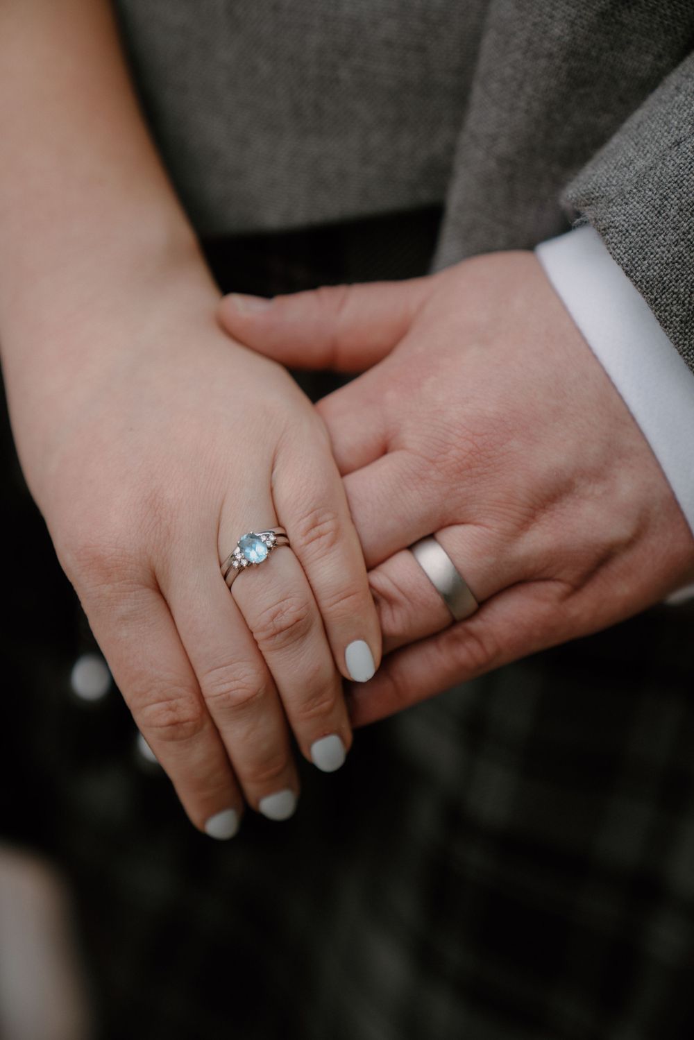 Close-up of wedding rings and clasped hands showing white nail polish.