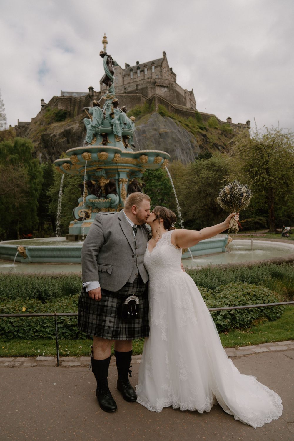 Couple takes selfie in front of Edinburgh Castle and ornate fountain.