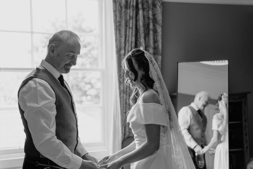Black and white photo of a bride and her father holding hands before the wedding ceremony.
